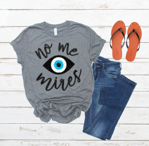 Flat lay of a gray shirt, jeans, and black sandals. Shirt says "No me mires" with an eye in the middle
