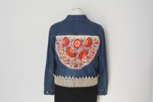 Denim jacket with colorful floral embroidery on the back. Lace trim around the bottom